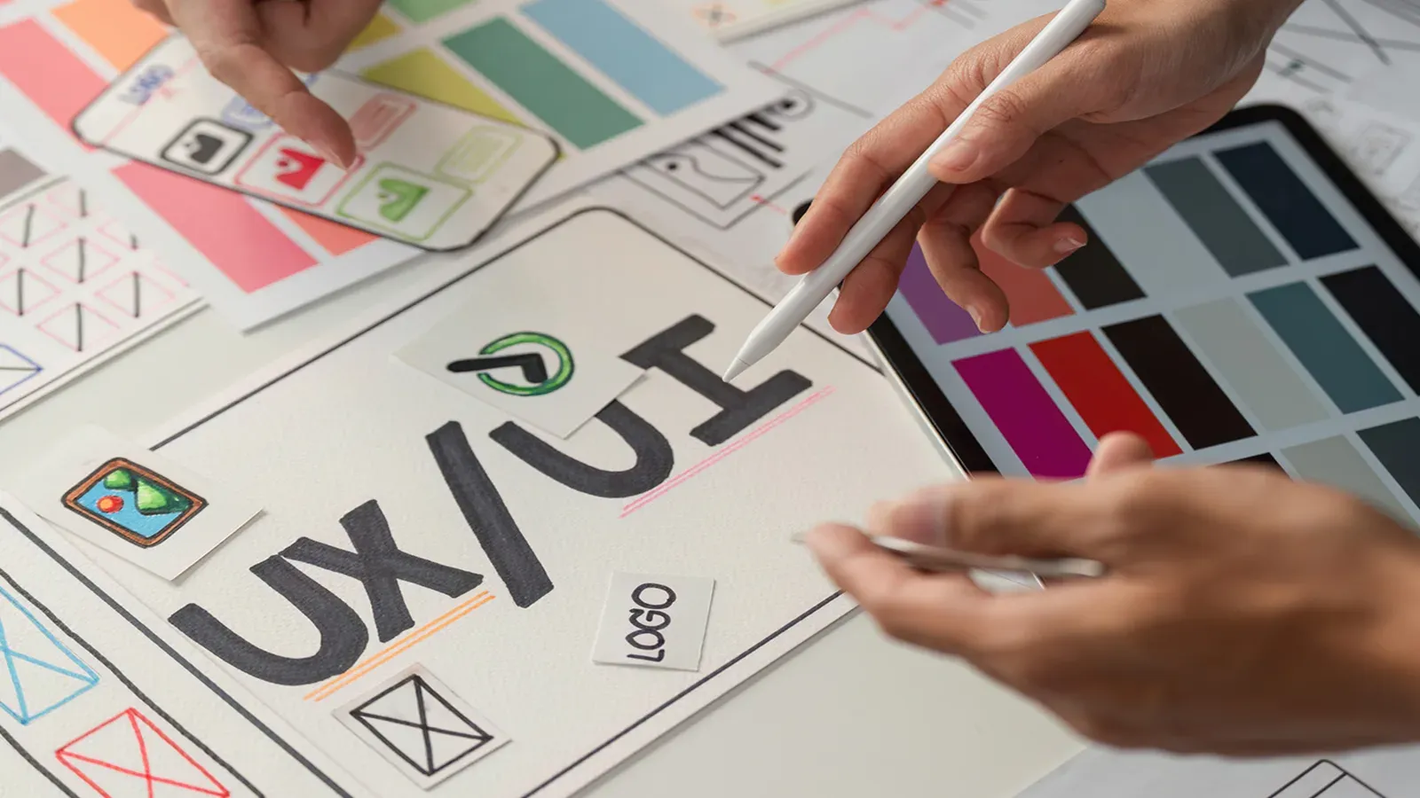 Designer esquissant une maquette d'interface UX/UI, entouré de palettes de couleurs et de croquis de logo