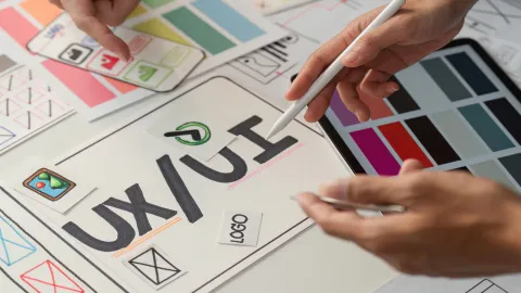 Designer esquissant une maquette d'interface UX/UI, entouré de palettes de couleurs et de croquis de logo